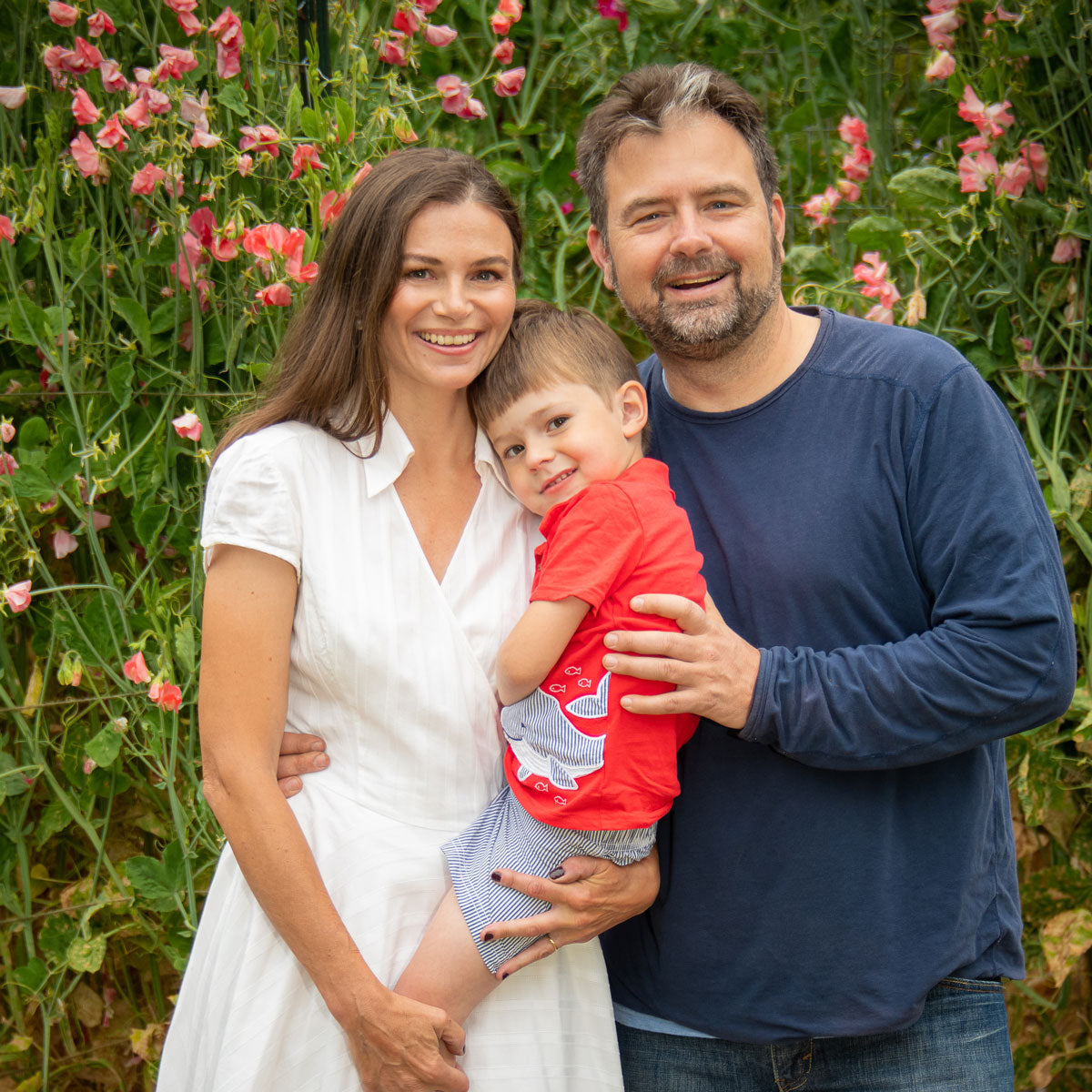 Founders of Sweet Pea Gardens standing among rows of blooming sweet pea vines on their farm – the family behind the heirloom seed collection.